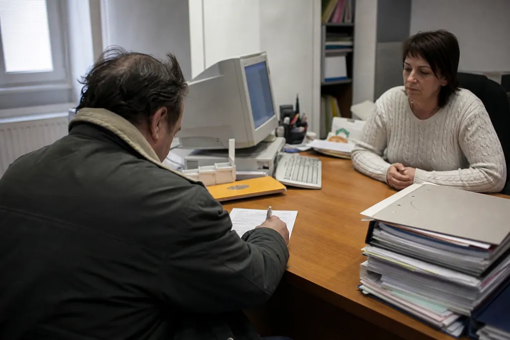 Un homme remplit un formulaire administratif face à une employée municipale