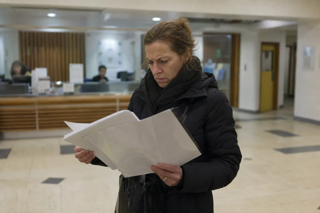 Une femme examine une pochette de documents dans le hall d'une mairie, l'air contrarié