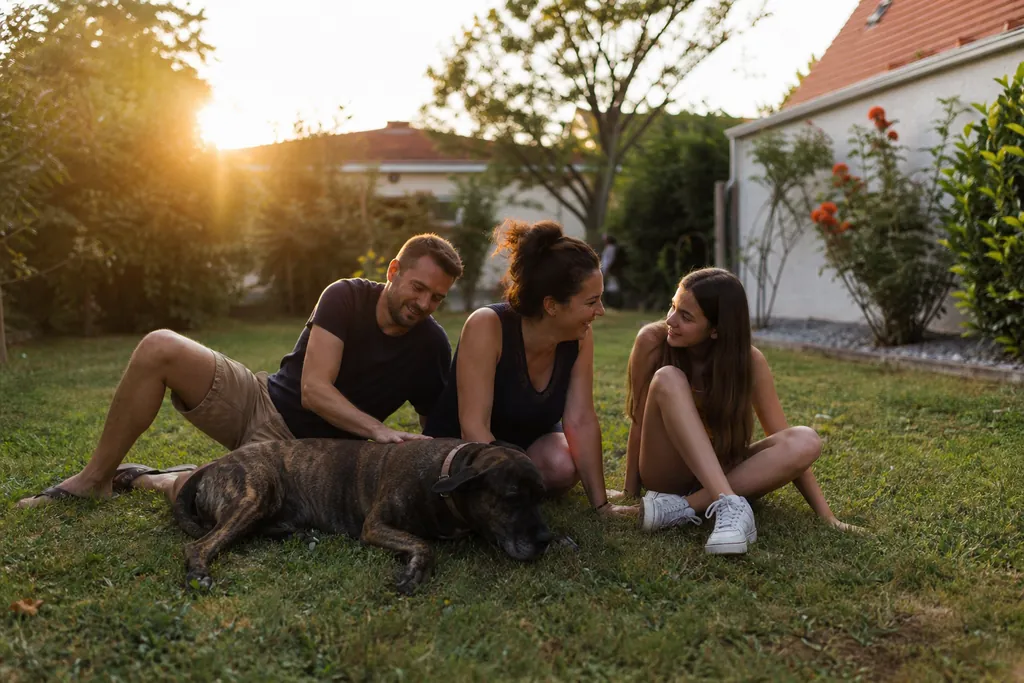 Une famille dans un petit jardin de pavillon, leur chien couché dans l'herbe à côté d'eux