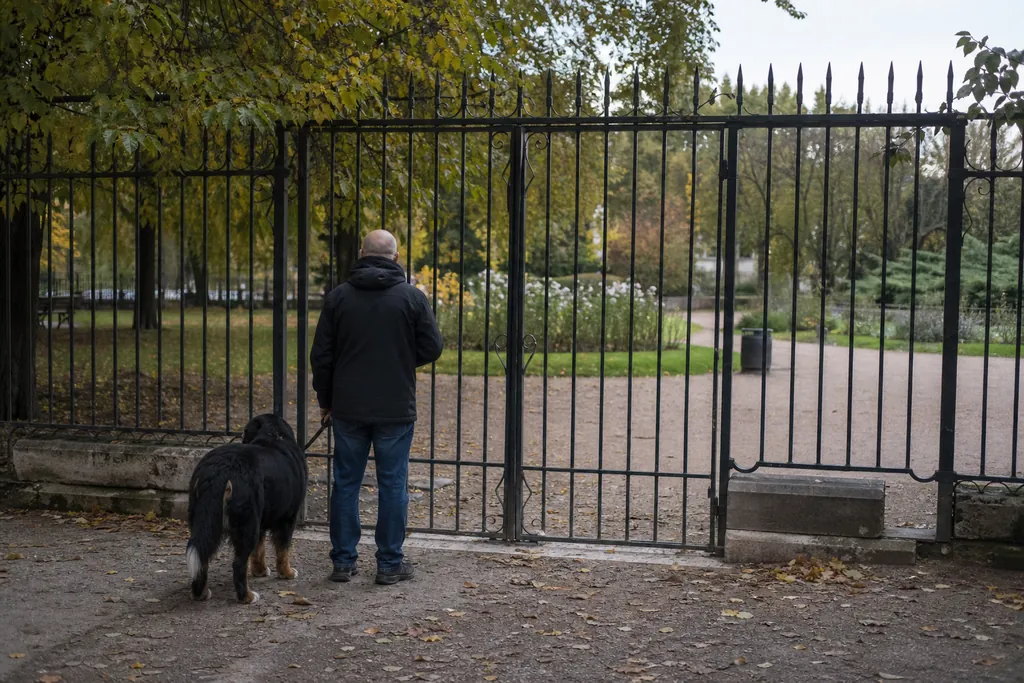 Un homme tient son chien en laisse devant la grille fermée d'un jardin public